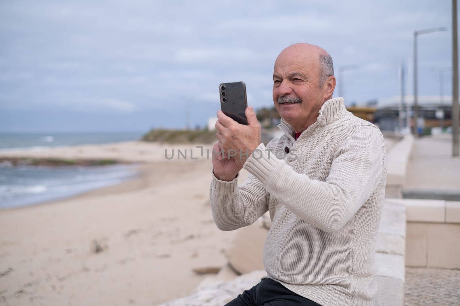An elderly person sitting by the ocean shore, taking photos of the view. Active retirement lifestyle.