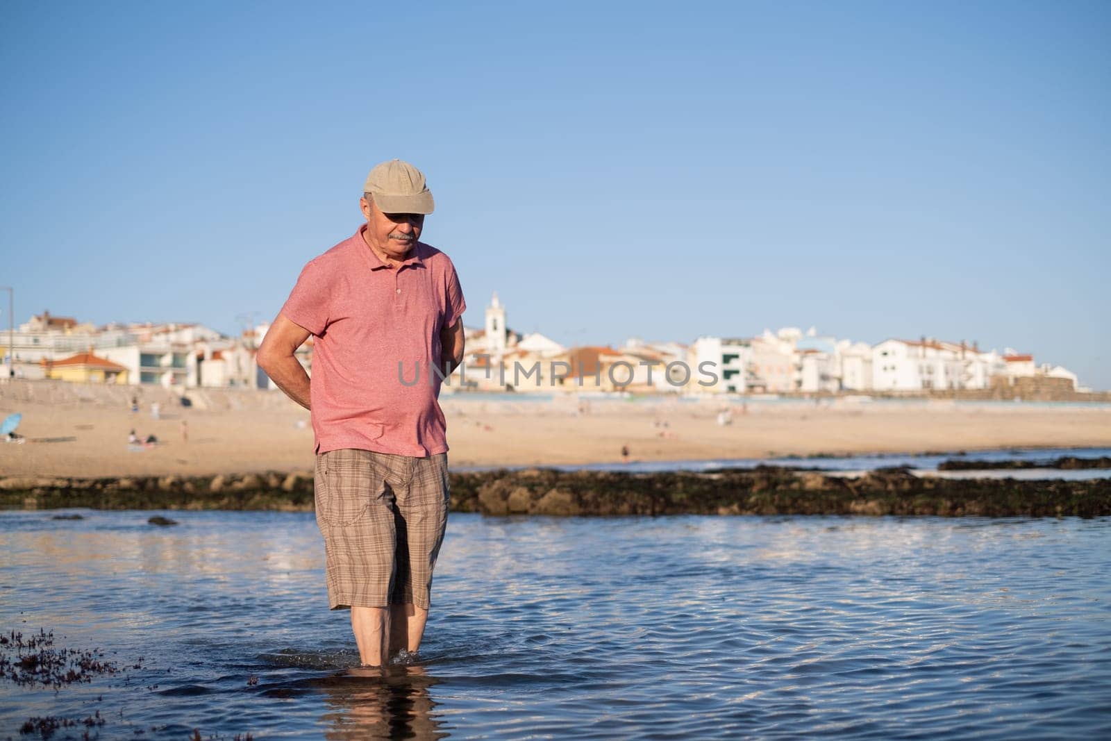 An elderly man with a mustache walking on the beach
