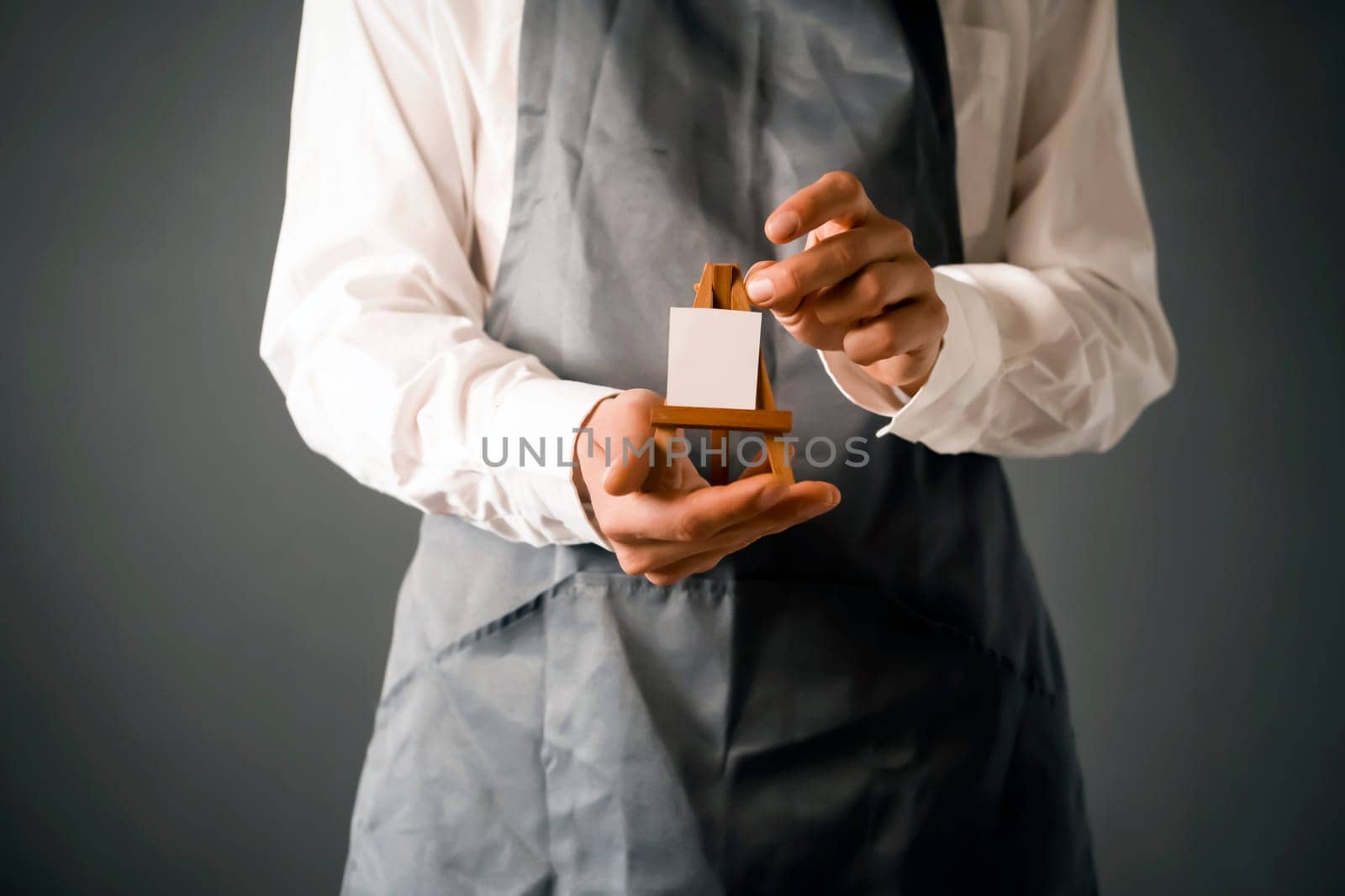The male artist's hands are holding a miniature easel with a small piece of white paper on it. A creative idea for inviting and discovering art.
