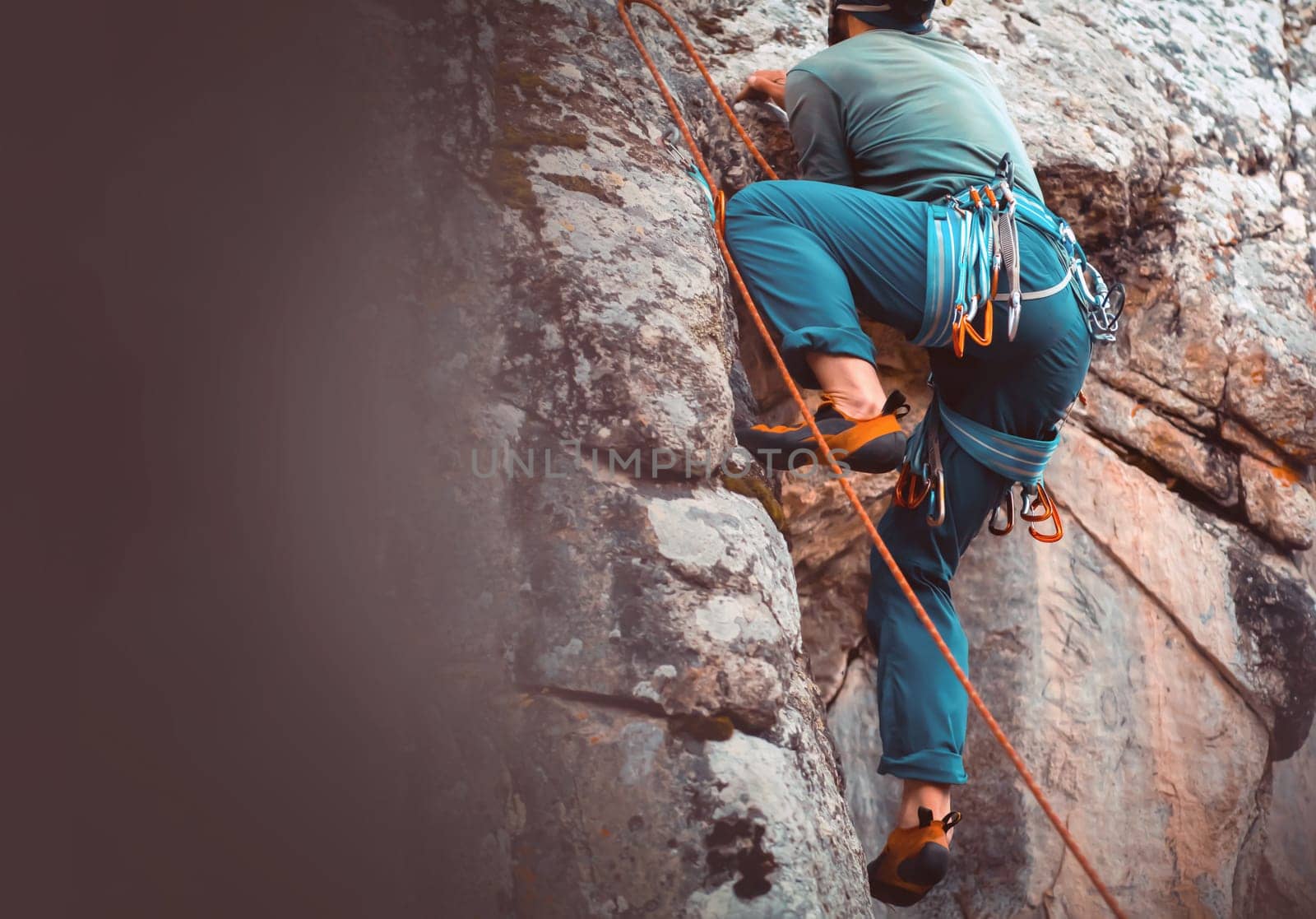 The young man is engaged in extreme sports, leads an active lifestyle, climbs a mountain, a rock with climbing equipment, wearing a helmet, with a rope, carabiners and climbing shoes.