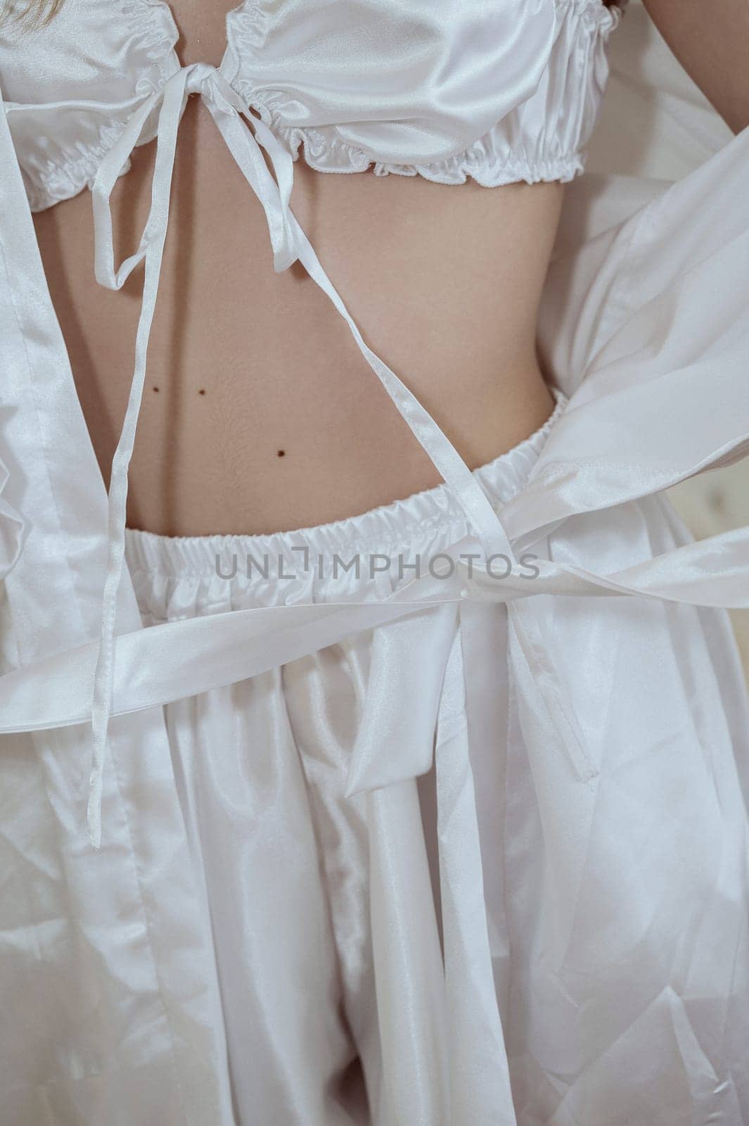 body of young girl in white silk lingerie and robe. part of body in underwear without face, close-up of waist