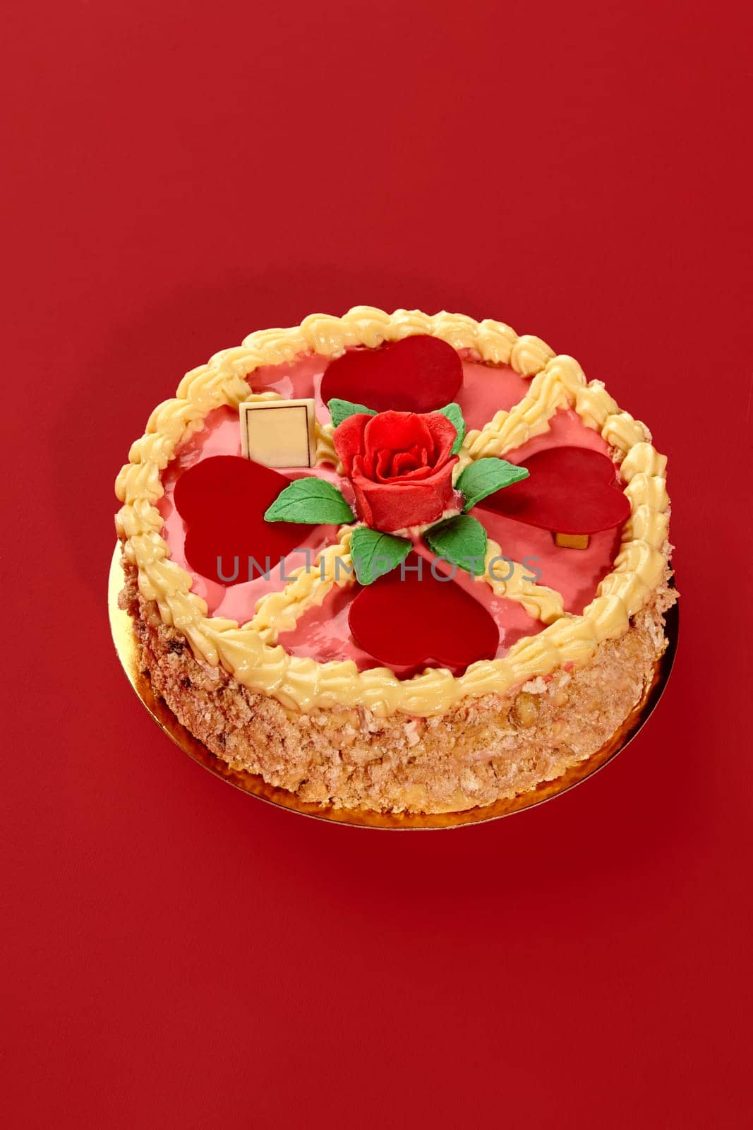 Round cake with pink icing, decorated with hearts, rose and green leaves, for braun family, on red background