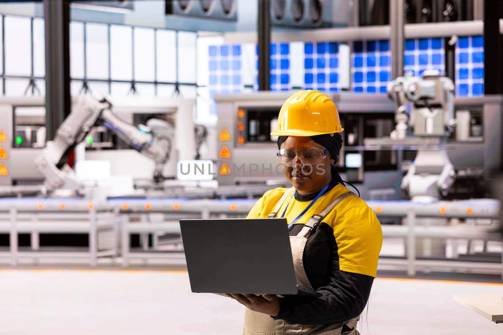 Female engineer in modern facility, overseeing operations and using laptop to ensure efficiency and safety. African american woman in factory, working on production of innovative devices.