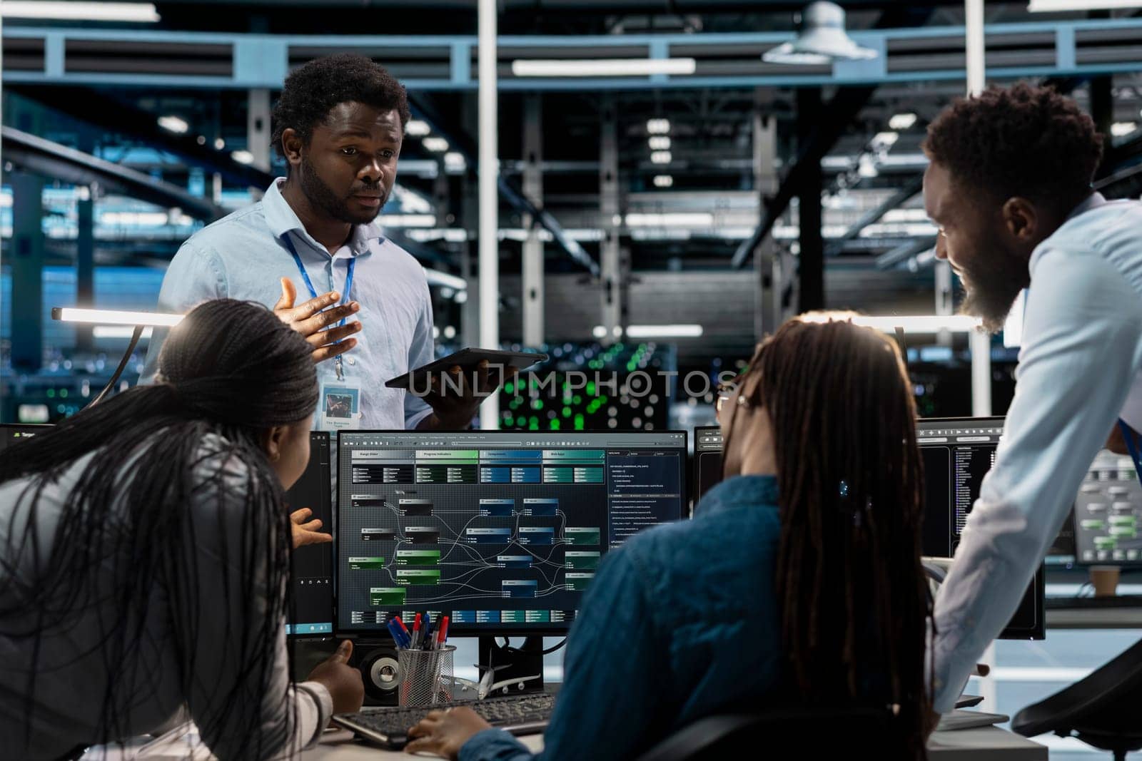 Engineers doing brainstorming, programming in server farm housing infrastructure storing datasets. Teamworking colleagues run code on PC to repair data center racks doing computational operations