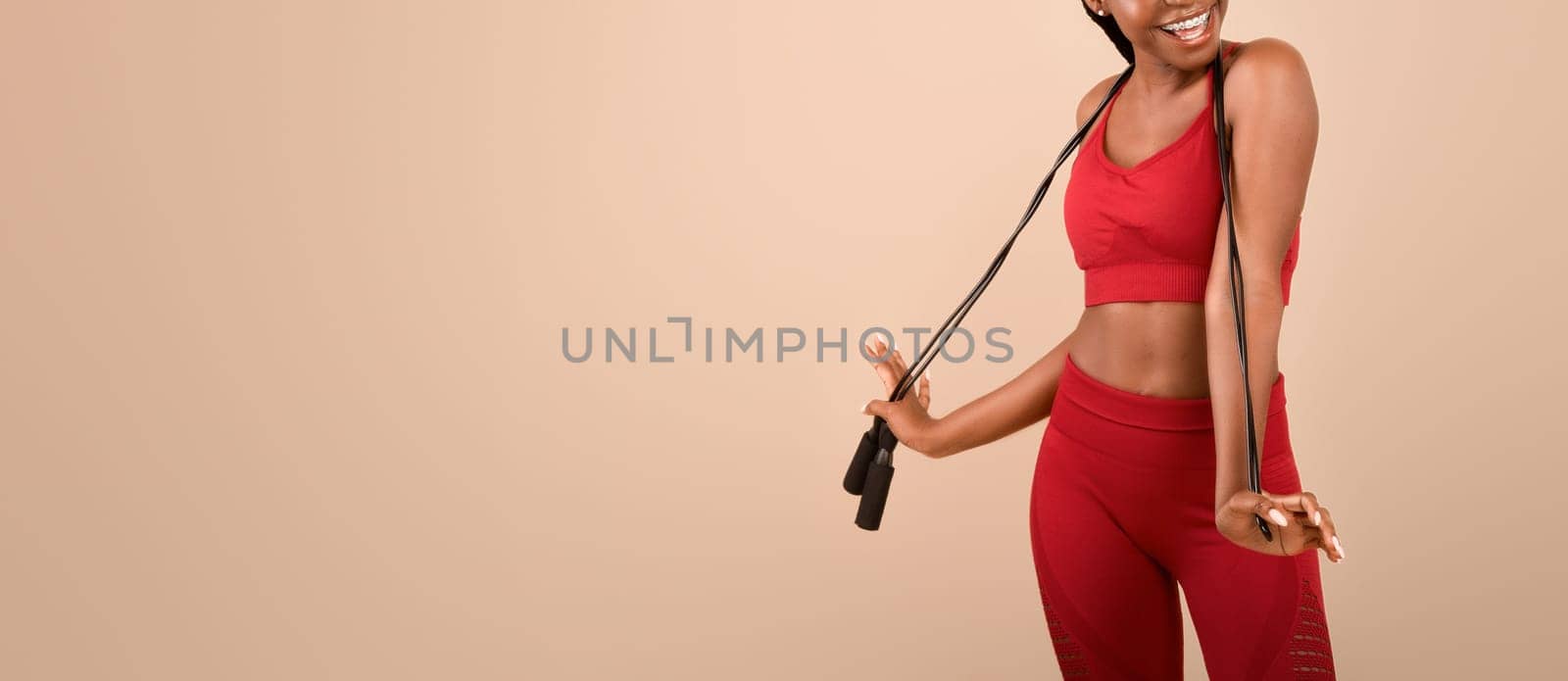 Fitness Concept. Portrait Of Joyful Fit Black Lady Posing With Jump Rope, Young Positive African American Woman In Sporty Clothing Standing Over Brown Studio Background, Enjoying Healthy Lifestyle