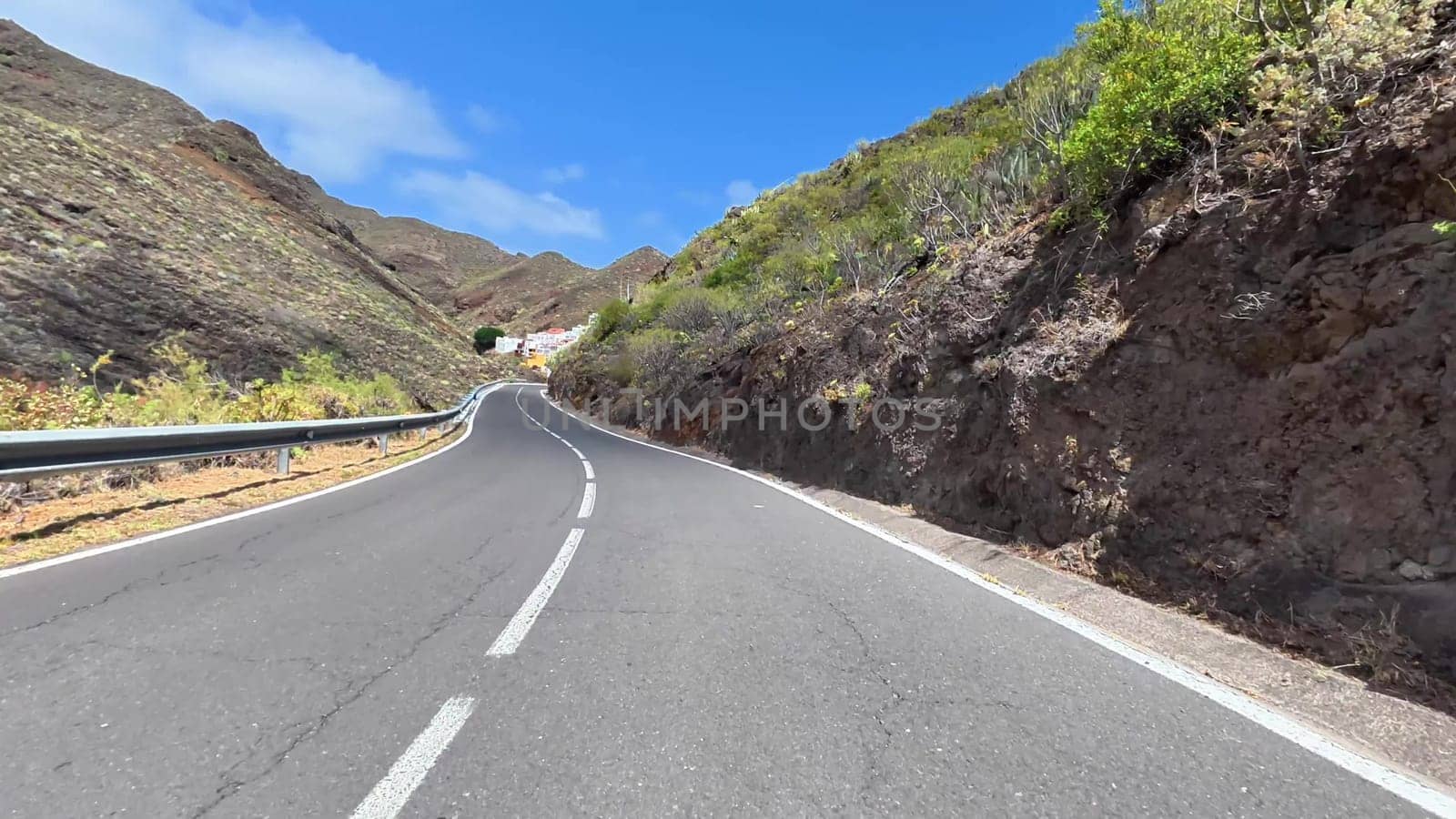 A scenic view of a winding road surrounded by majestic mountains and lush greenery under a clear blue sky
