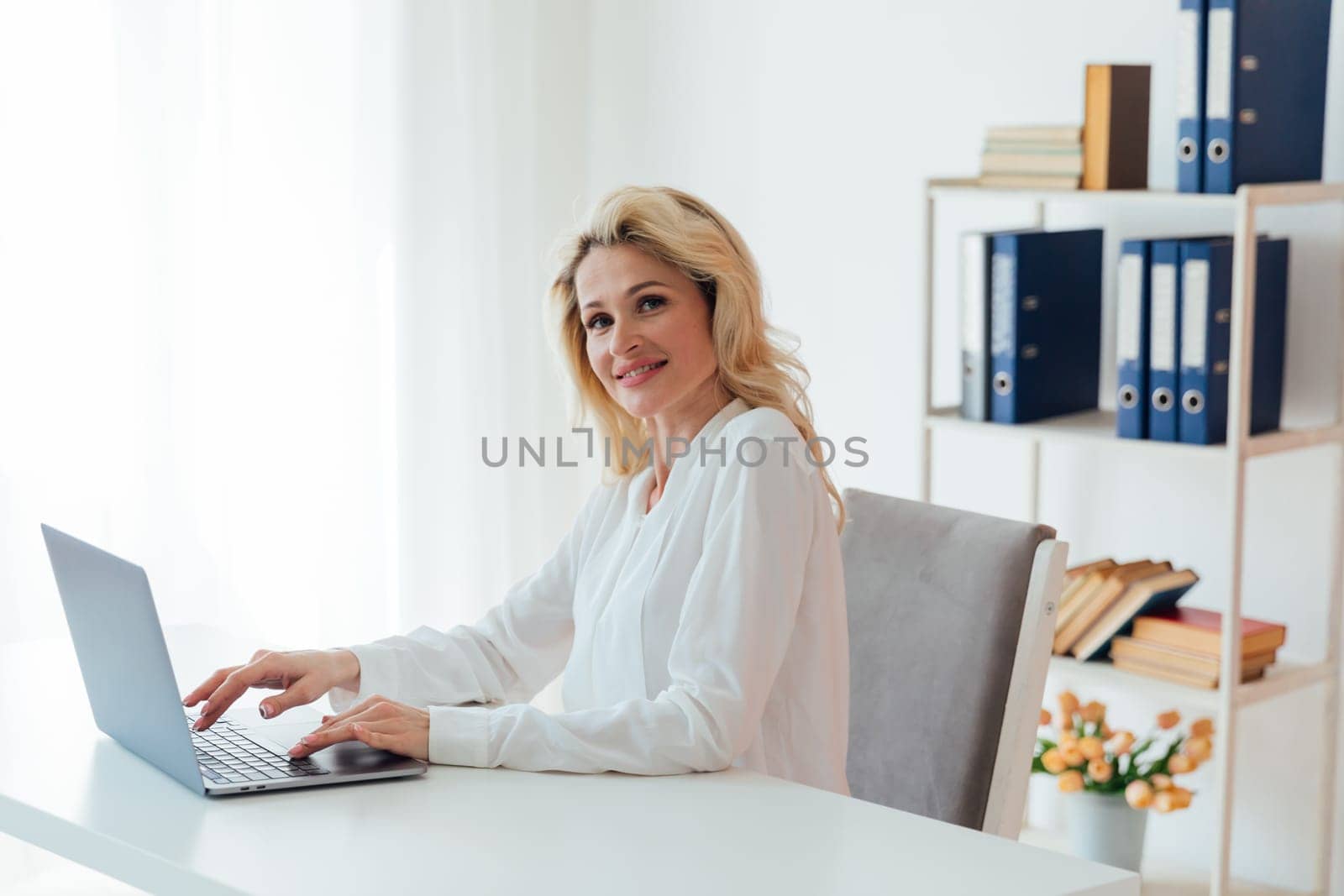 Blonde business woman working on laptop at desk in office online