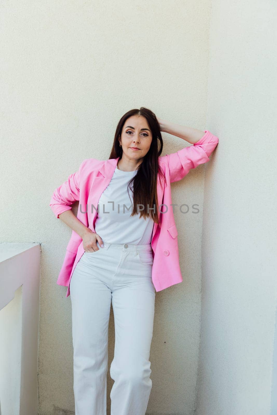 Beautiful fashion brunette woman in white clothes and pink jacket on light background