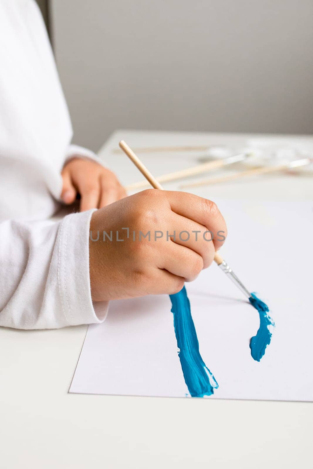 Young caucasian child painting with blue brushstroke on white paper.
