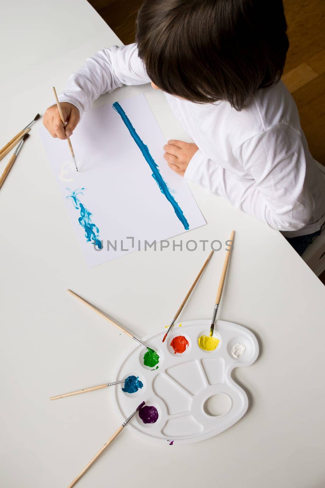 Young caucasian child painting with watercolors at home.