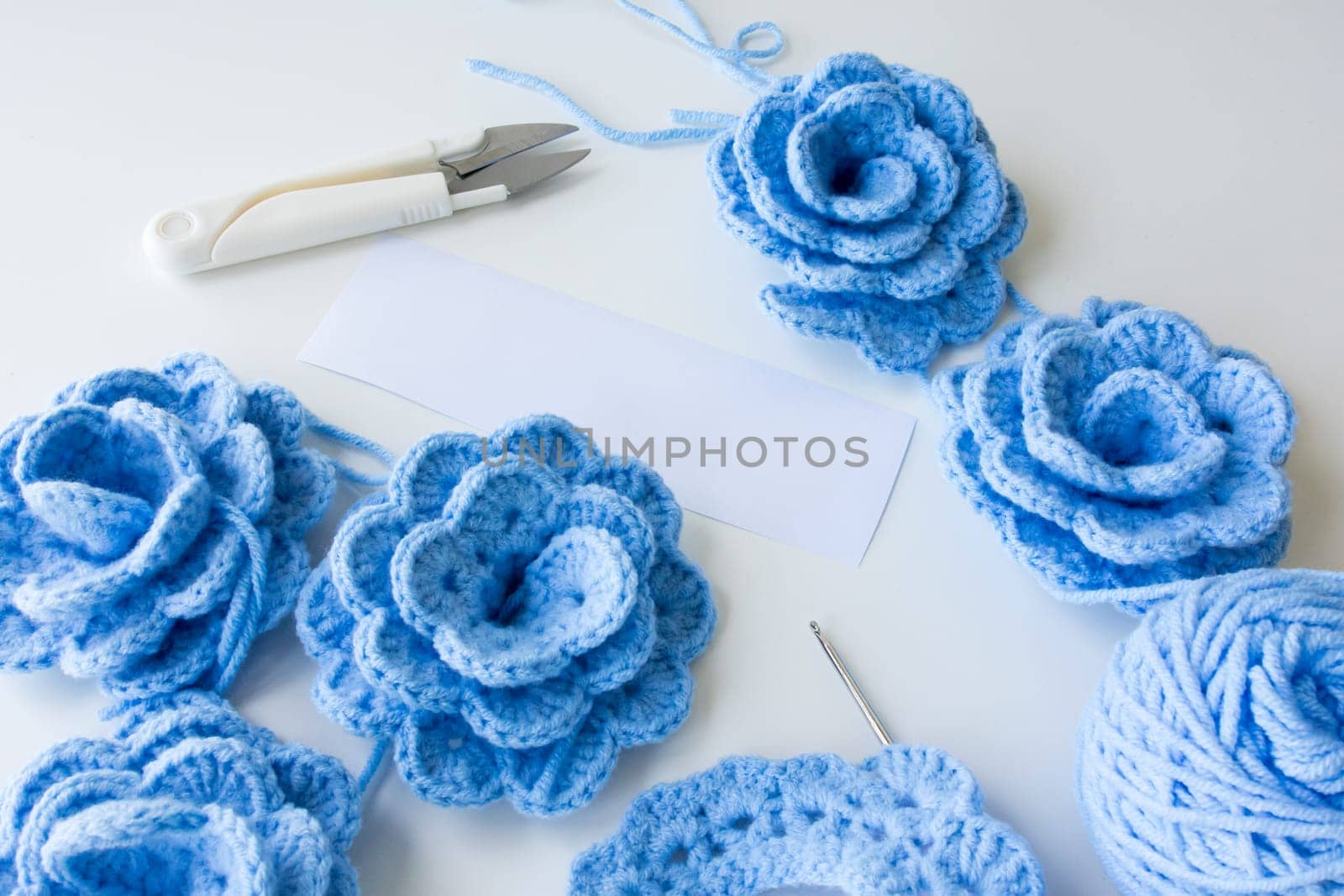 Blue crocheted flowers with yarn and tools on white background. High quality.