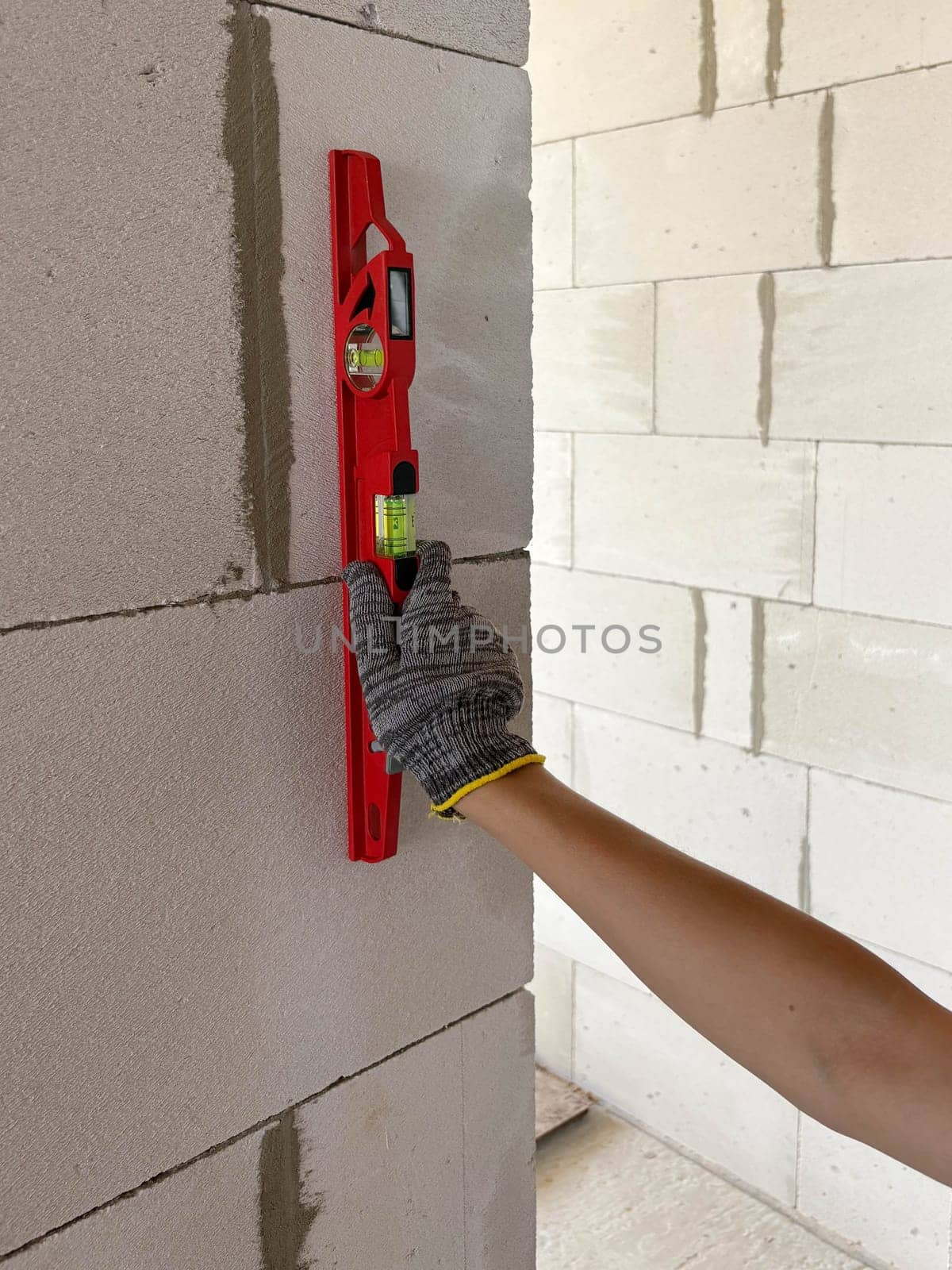 A builder applies a bubble level to a new wall at a construction site to check its levelness. Measuring tools at the construction site.