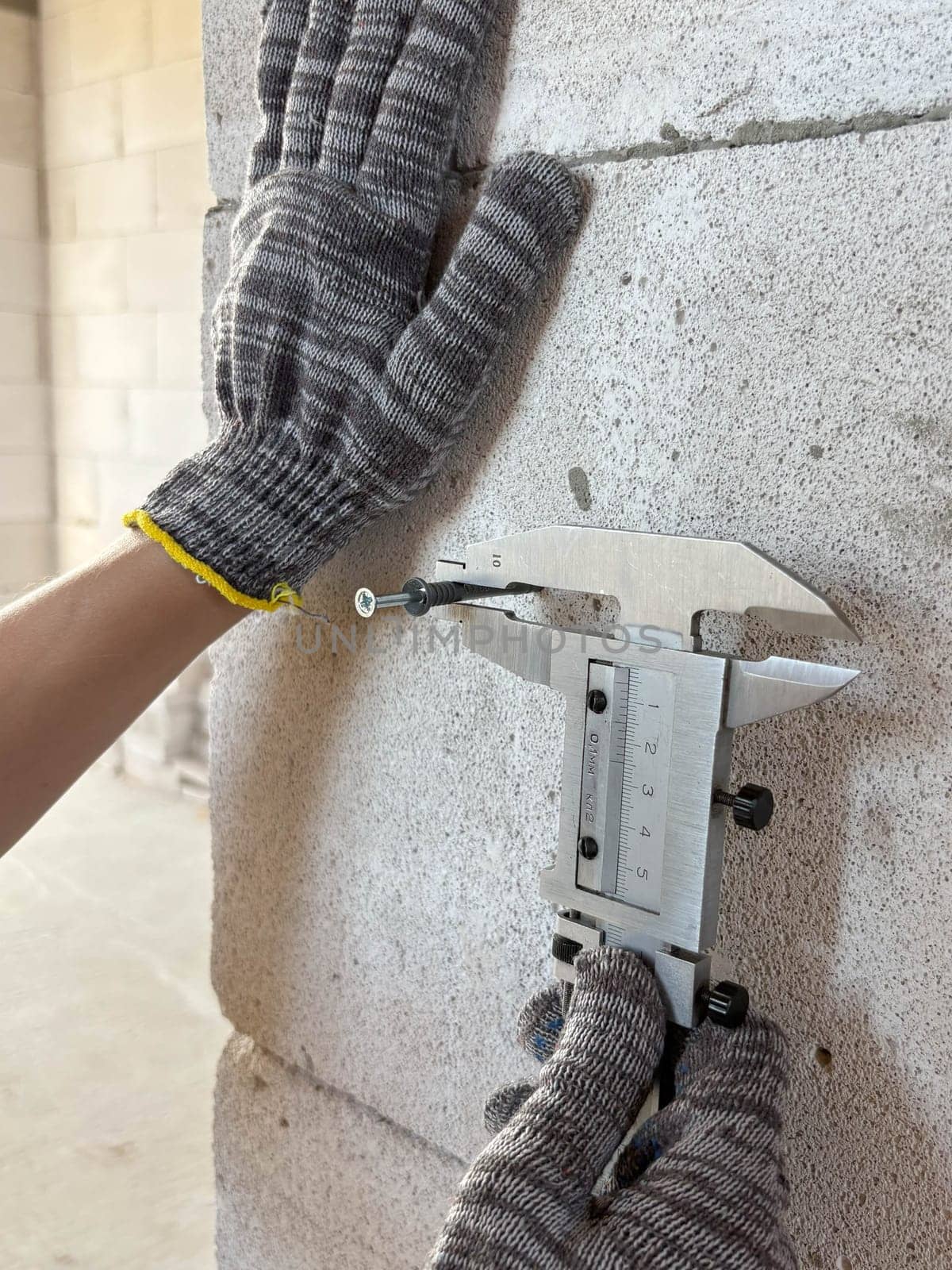 Metal caliper, construction and working measuring tool. Worker's hands measure the diameter of a dowel in a wall with a caliper. Construction and renovation concept.
