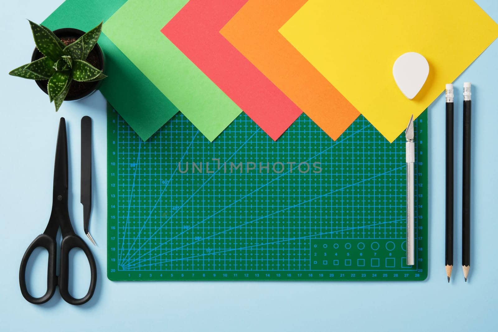 Paper crafts work table flatlay. Tools for hobby, green cutting mat, scissors, craft knife, pencil, eraser, colored paper. Space for your text.
