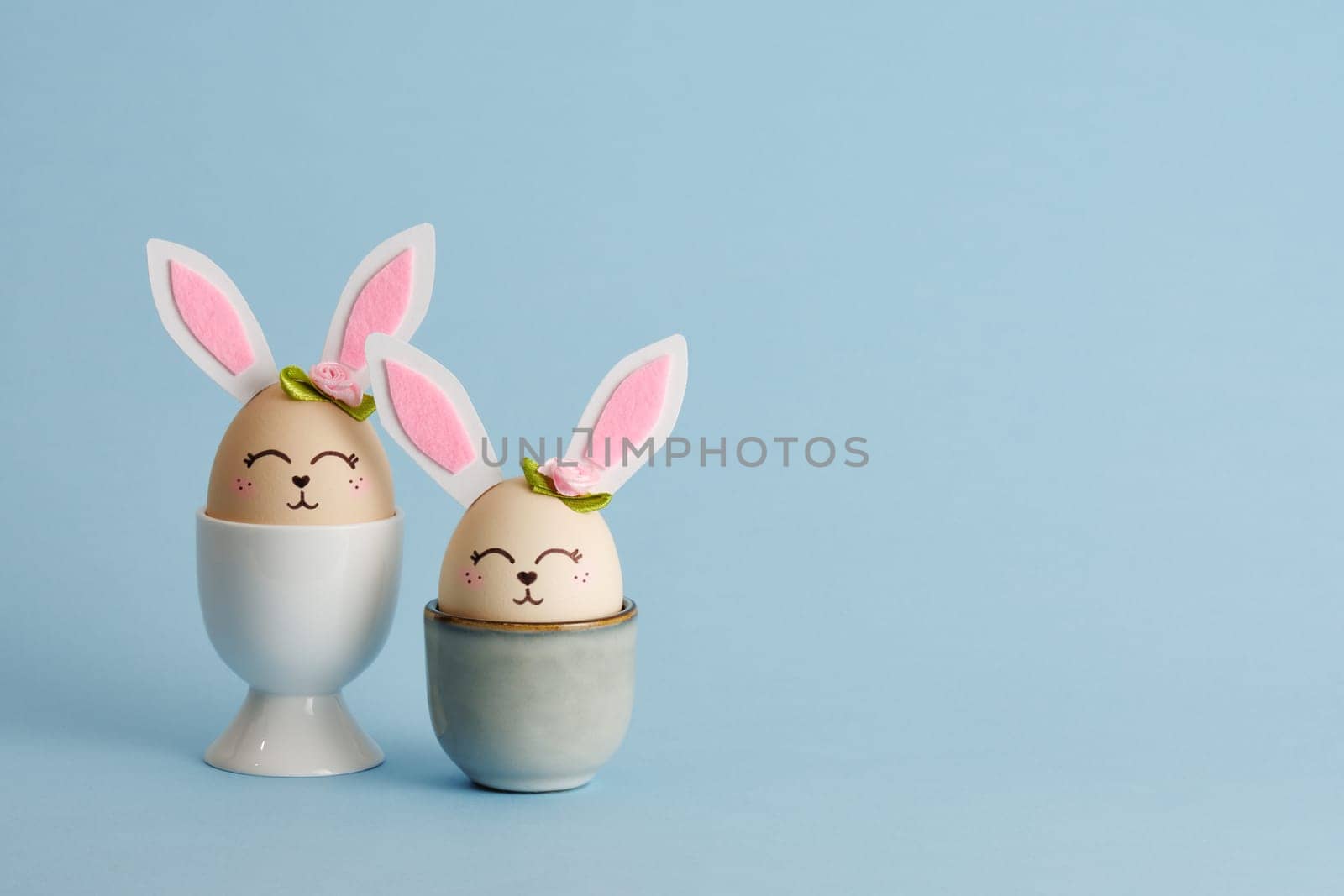 Cute Easter bunny shaped eggs in egg holders on blue background. Place for your text