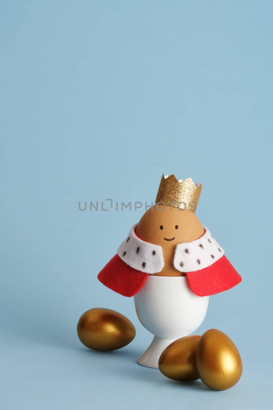 A craft Easter egg of a king with a crown and red robe on a blue background. Idea for children's creativity.