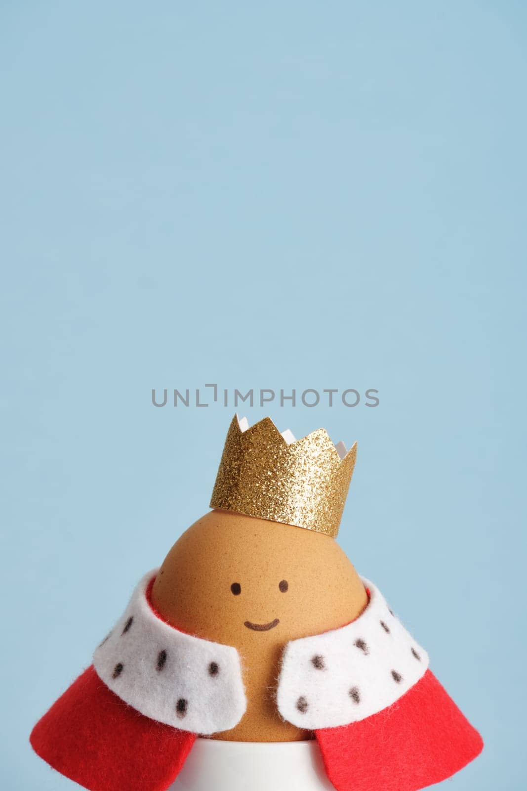 Easter egg featuring king with crown and red robe close up on blue background. Place for your text.