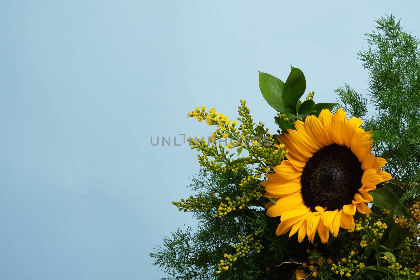 Brightly colored bouquet with yellow sunflower and green foliage on a blue background. Place for your text.