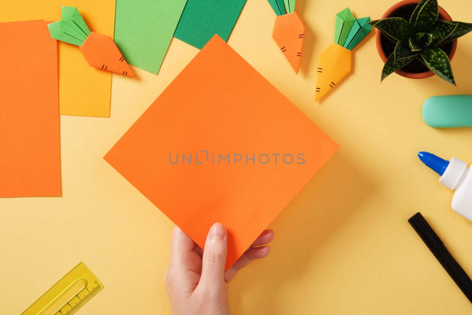 Making a simple origami carrot Easter craft. Take a square sheet of orange or yellow paper. Around the paper creativity tools.