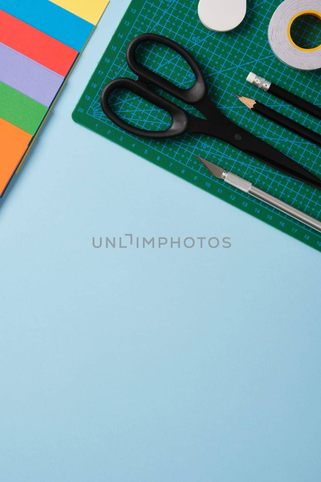 Supplies for paper art hobby: scissors, craft knife, pencil, eraser, colored paper. Space for your text. Paper crafts work table flatlay.