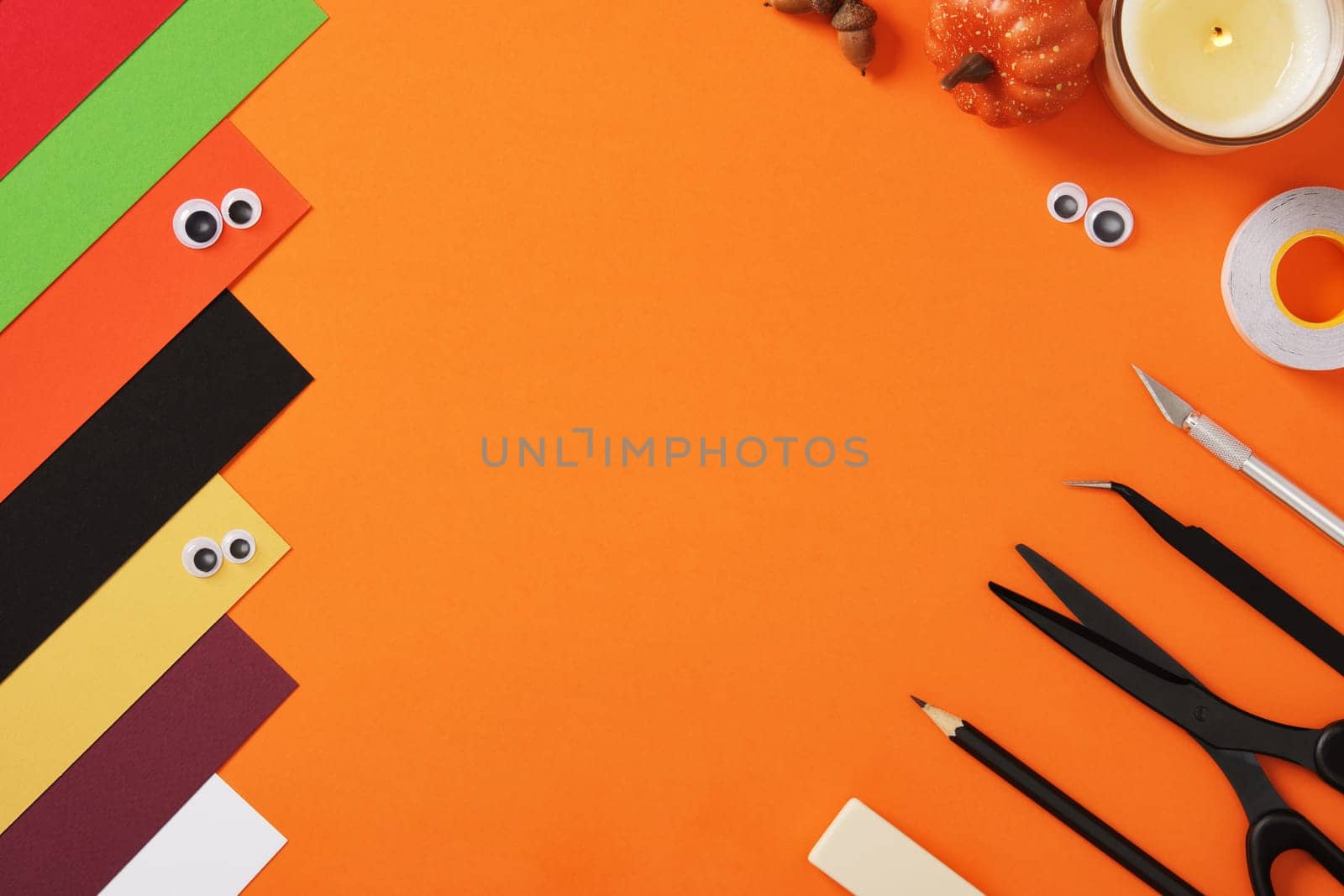 Supplies for paper crafts in Halloween colors. Pencil, eraser, knife, scissors, tape and colored pieces of paper.