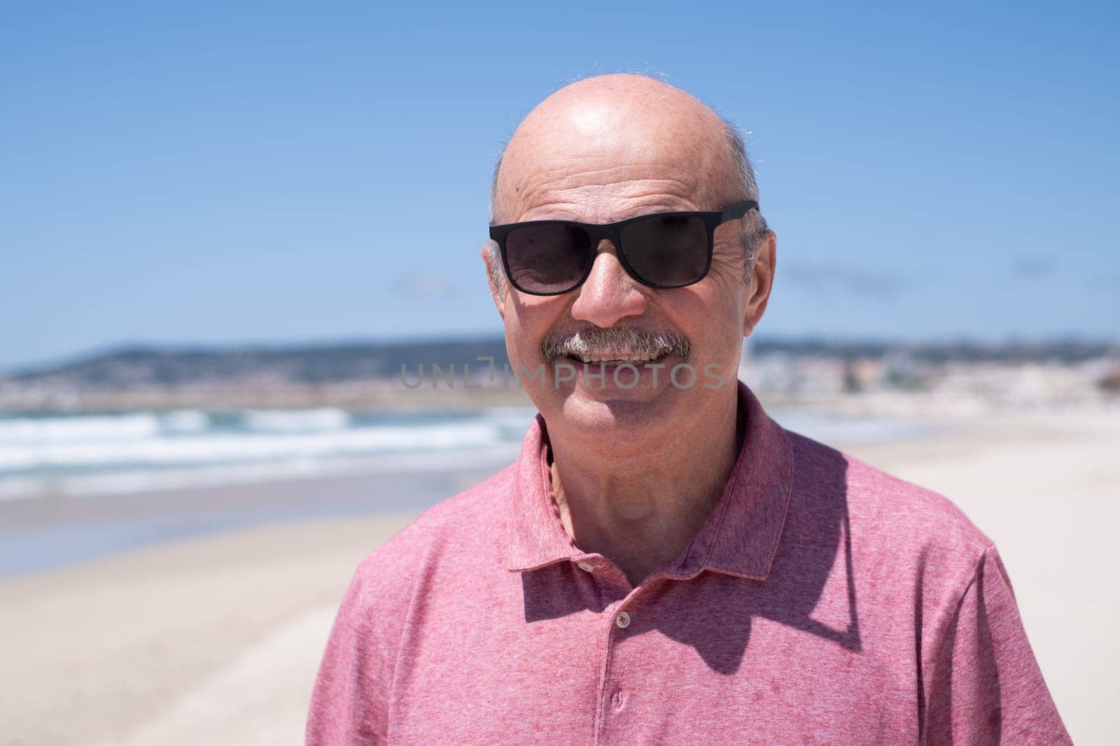 An elderly man with a mustache walking on the beach