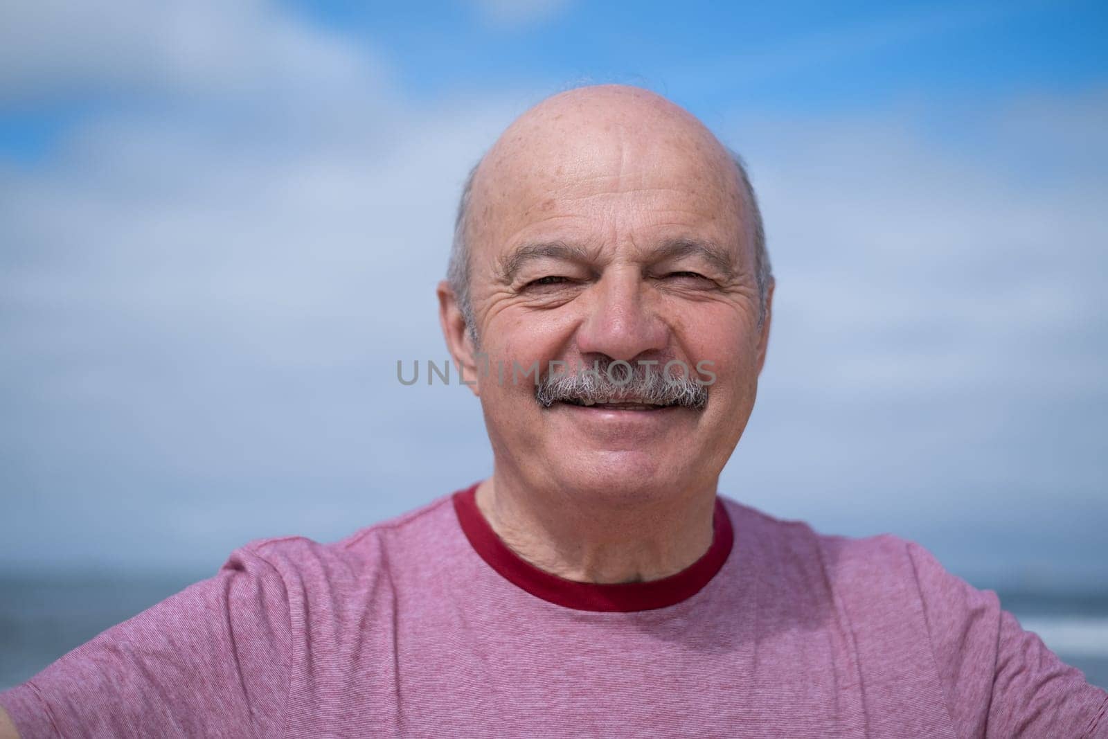 An elderly man with a mustache walking on the beach