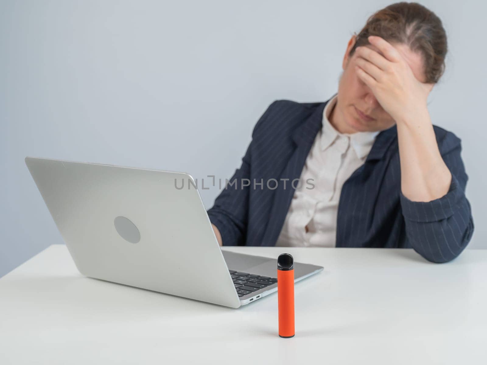Caucasian businesswoman working on laptop. Disposable vape in foreground