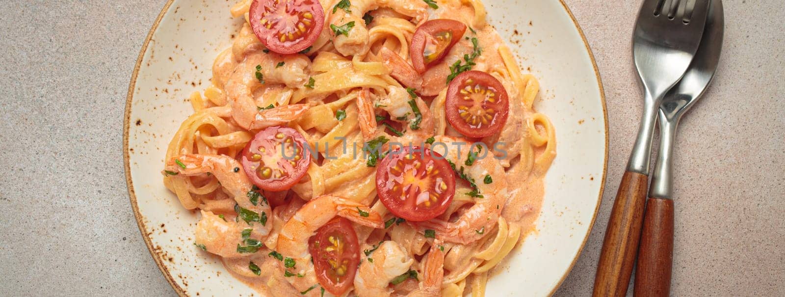 Seafood linguine pasta in creamy sauce with shrimp and cherry tomatoes, garnished with fresh parsley, served on a light warm beige background with cutlery top view