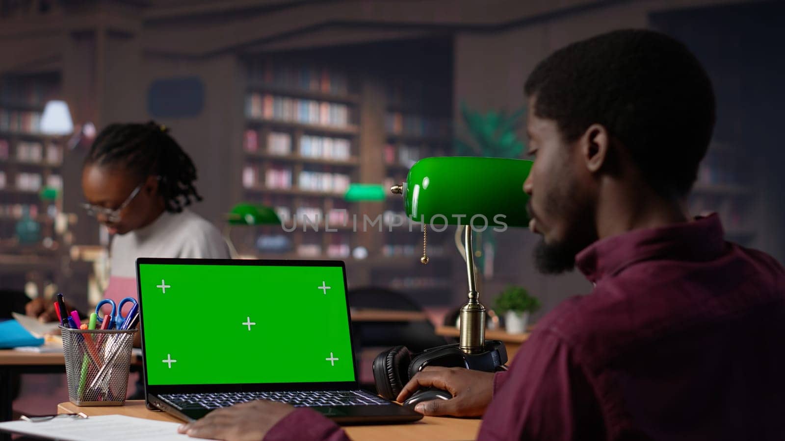 College student looks at a copy space on laptop while collecting notes from reliable academic sources, consulting the campus library books collection for an assignment. Student life. Camera A.