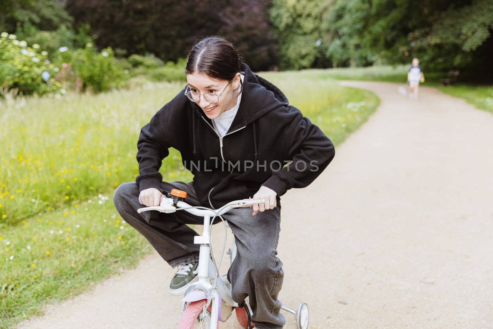 Portrait of a beautiful Caucasian teenage girl having fun and fooling around riding a small children's bicycle in a park on a spring day, side view close-up. Concept happy fooling around, sports games in the fresh air.