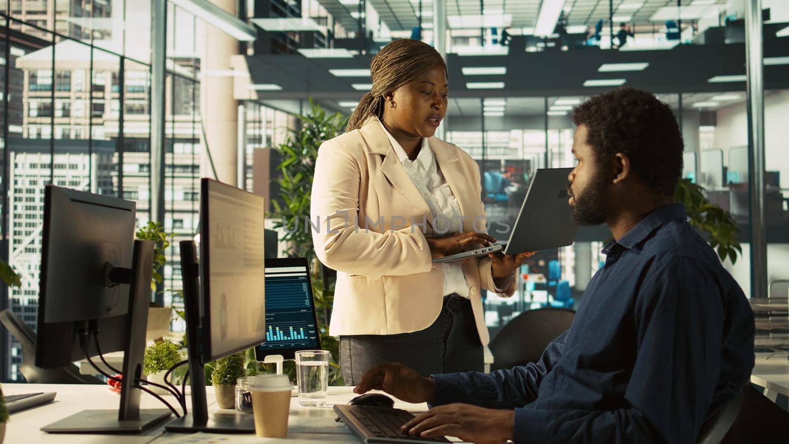 Worker in office receiving feedback from management executive looking over work done on laptop. African american manager in workspace giving tasks to employee, providing necessary data, camera B