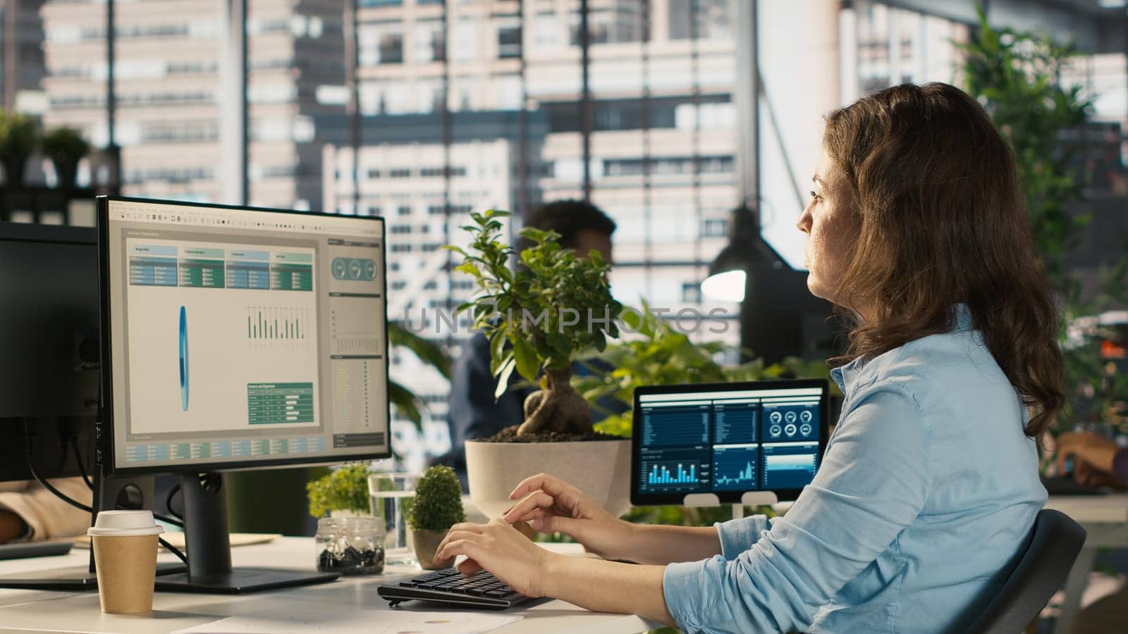 Accountant in busy modern startup agency imputing financial figures on PC after checking reports. Focused businesswoman working in modern office, crosschecking data, camera A