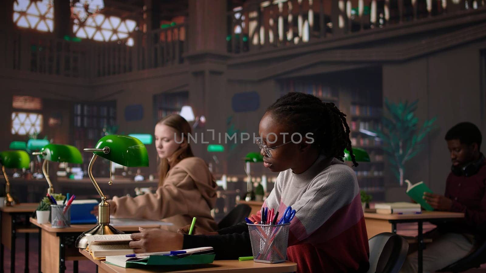 University student engrossed in texting with classmates at the library, chatting with friends instead of studying. Girl discussing with colleagues about an assignment. Camera B.