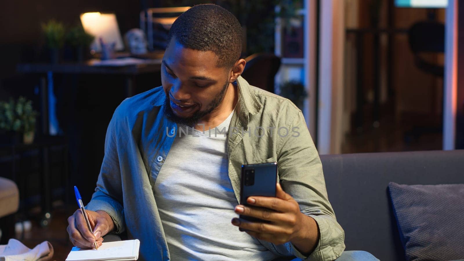 African american teleworker calling coworker on video conference to take notes, writing new ideas and exchanging information on web meeting in the living room. Textbook data. Camera B.