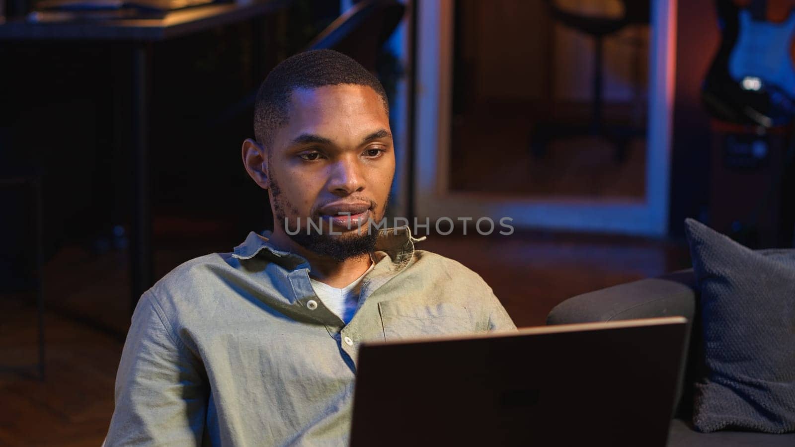 Black male freelancer taking online course to learn new skills from home, attend online video call and watching lecture from loft. Young man participates at a virtual training class. Camera B.
