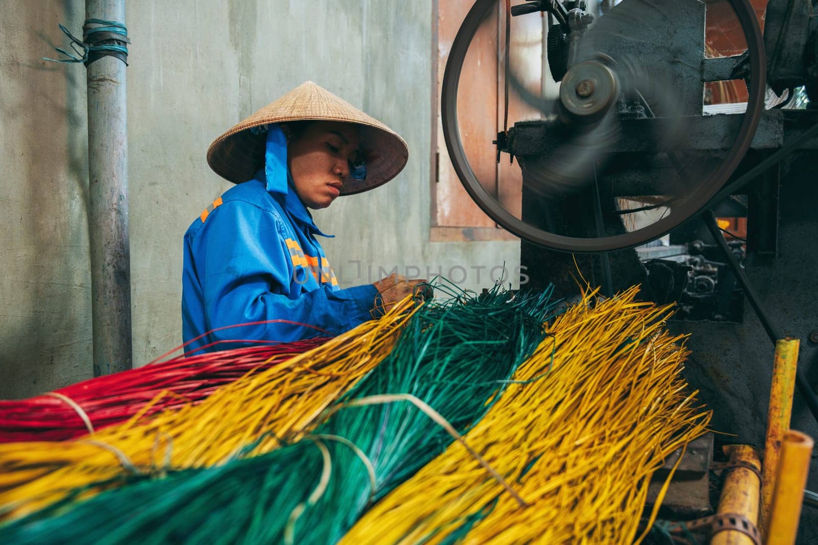Vietnamese woman in a straw hat works at a loom in a factory for the production of woven reed mats. An Cu, Tuy An, Phu Yen province, Vietnam - April 14, 2025