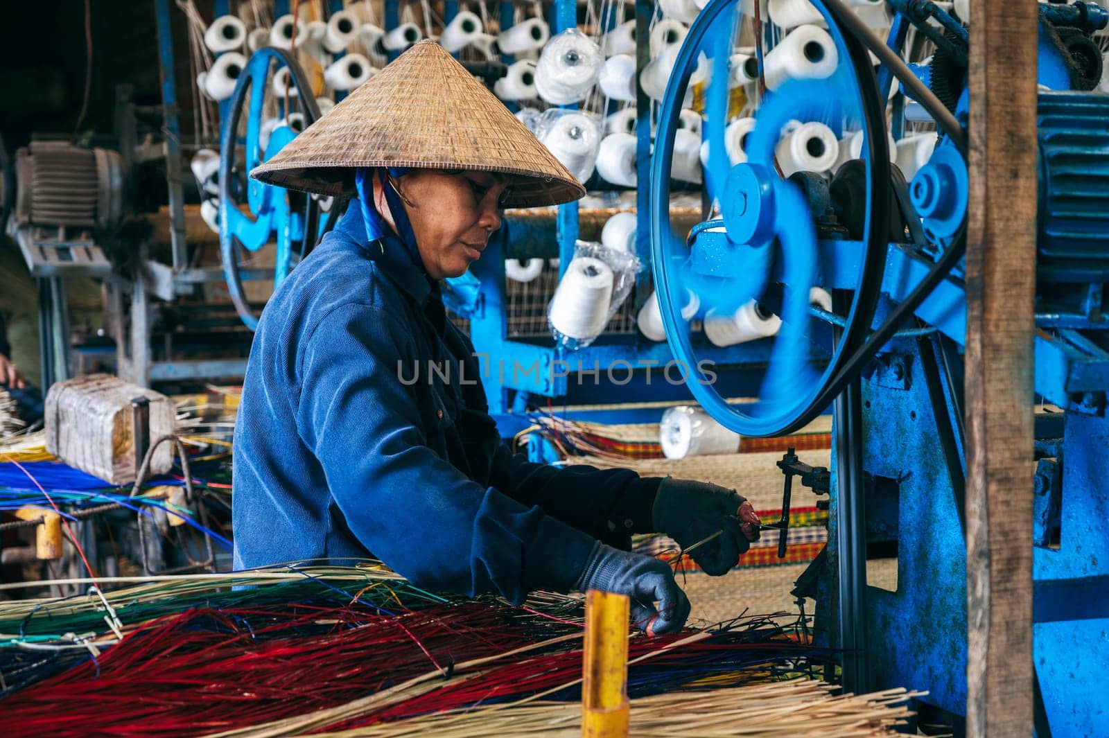 Vietnamese female weaver works on loom in workshop at factory producing traditional woven reed mats in Vietnam. An Cu, Tuy An, Phu Yen province, Vietnam - April 14, 2025