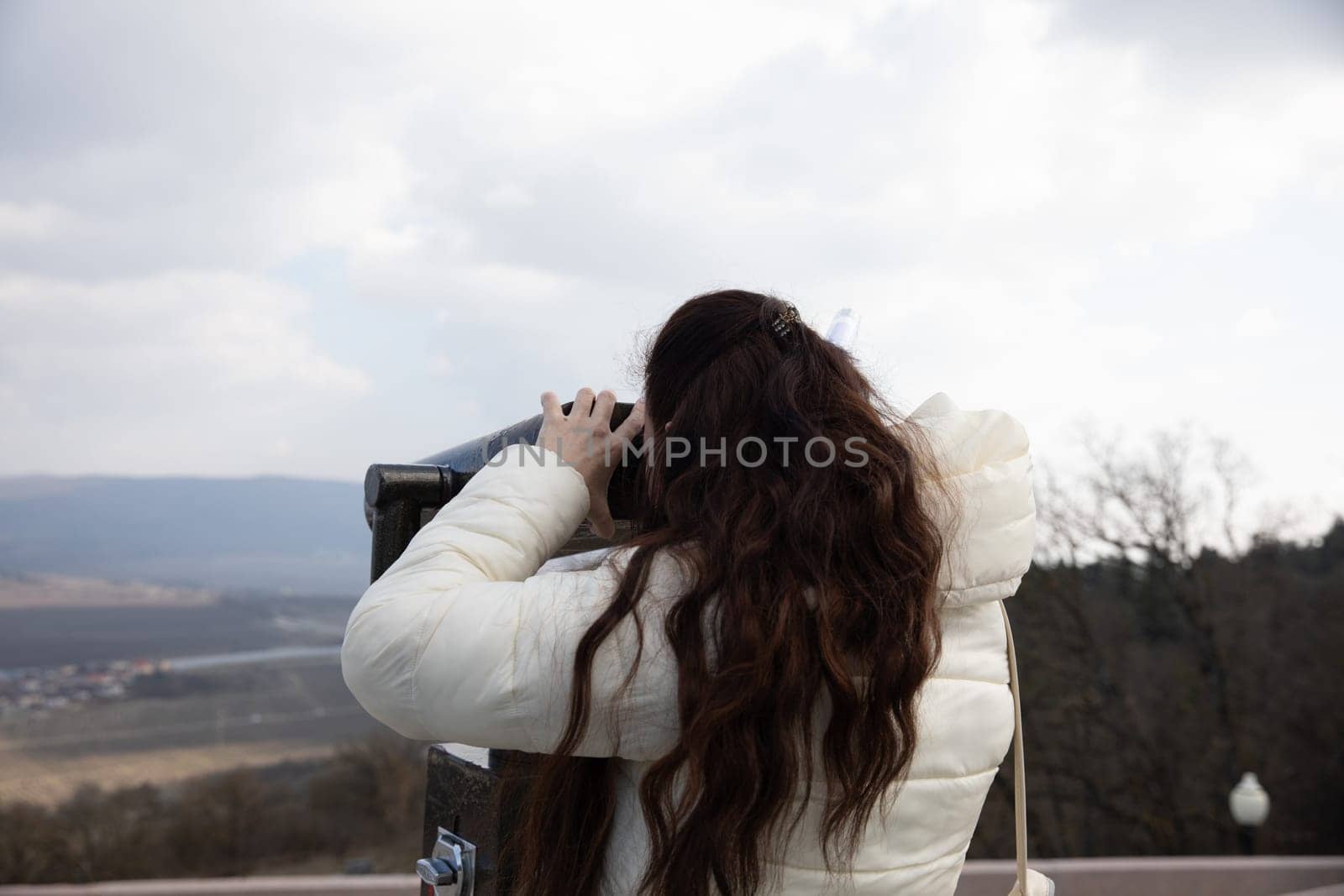 Woman looking through binoculars from the top of a mountain at the landscape