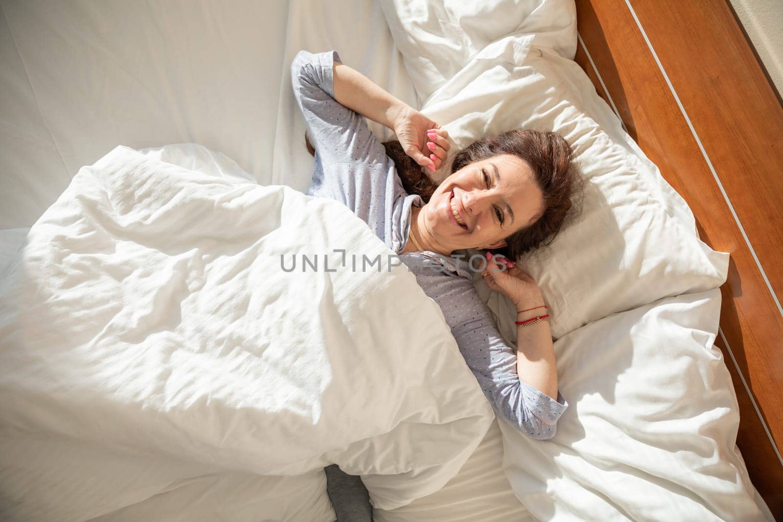 Brunette in pajamas woke up in the morning in the bedroom on the bed smiling