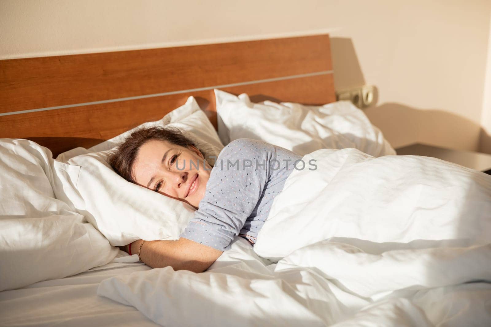 Brunette in pajamas woke up in the morning in the bedroom on the bed smiling