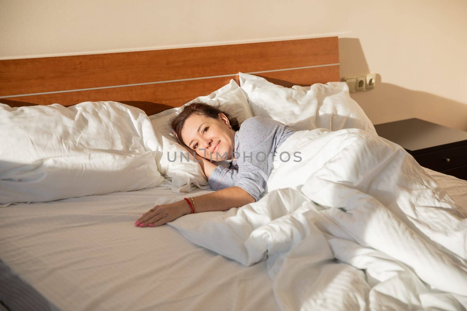 Woman in pajamas sleeping under blanket in the morning in bedroom on bed