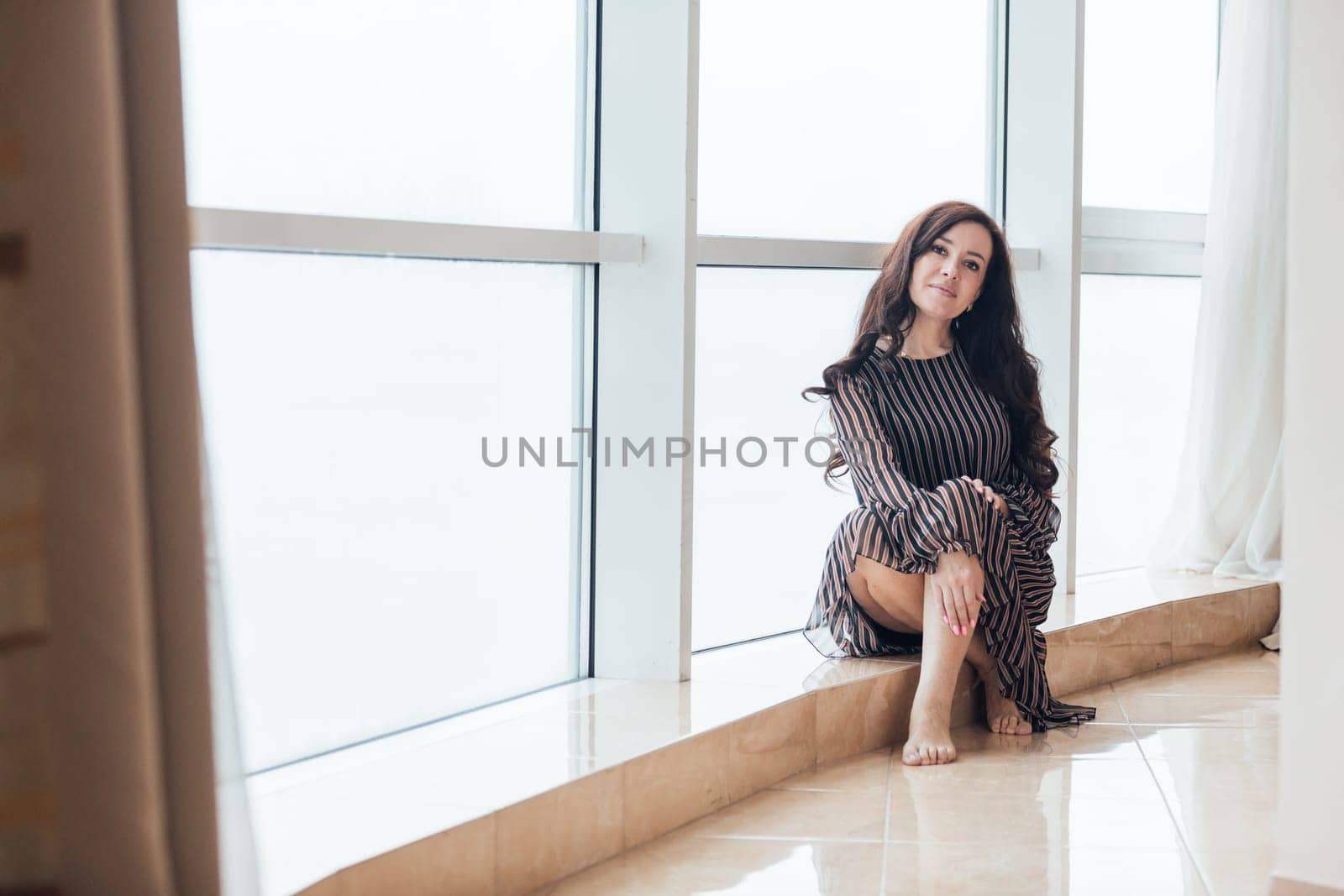 Beautiful woman 40 years old at the window in the interior of the room
