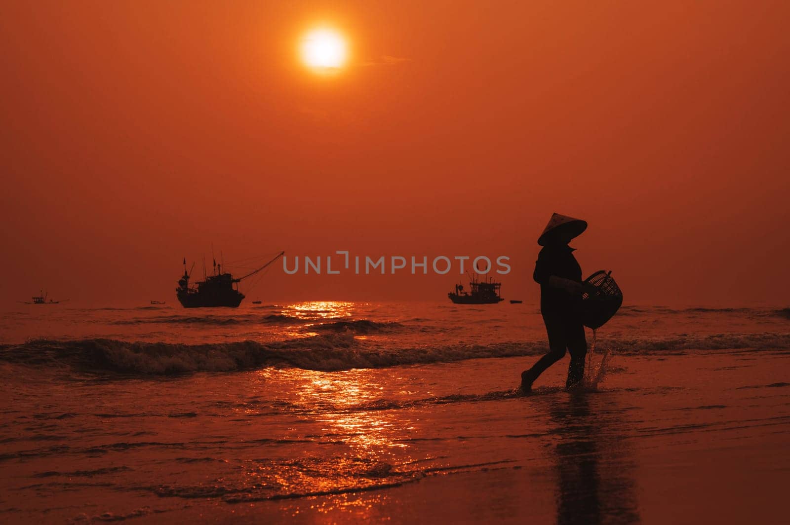 Silhouette of Vietnamese woman in straw hat on the shore of sea with ships in fishing village in morning at sunrise in Vietnam