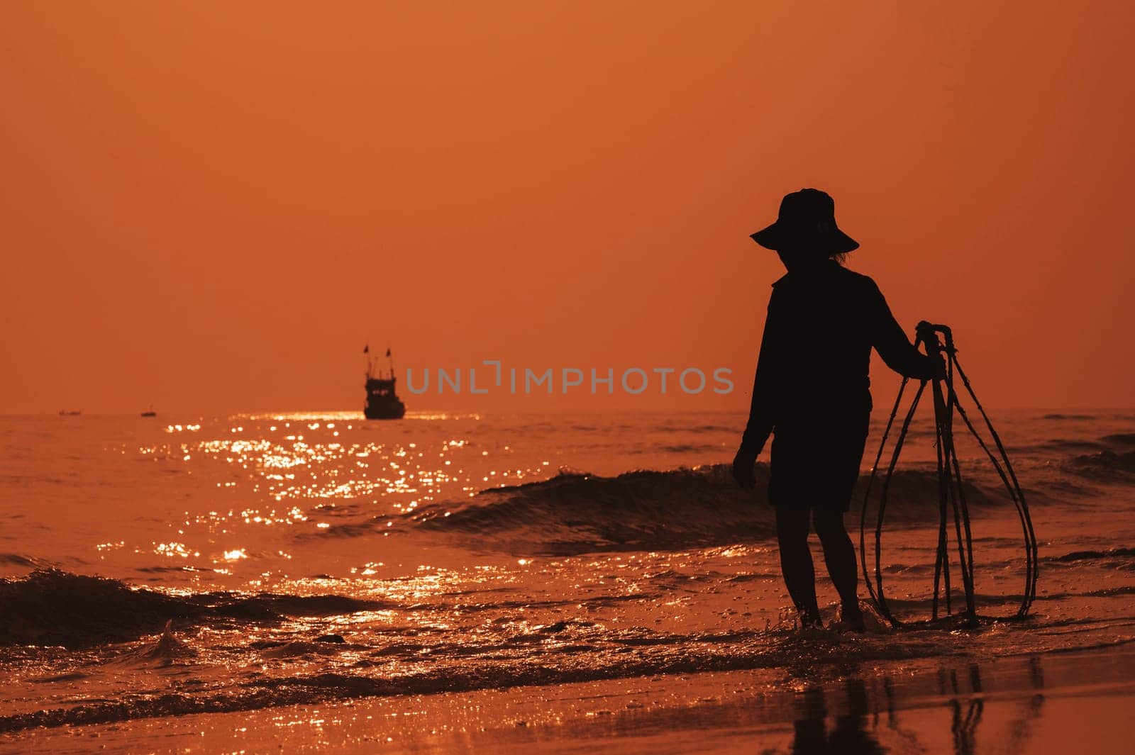 Silhouette of Vietnamese woman on the shore of sea with ship in a fishing village in morning at sunrise in Vietnam
