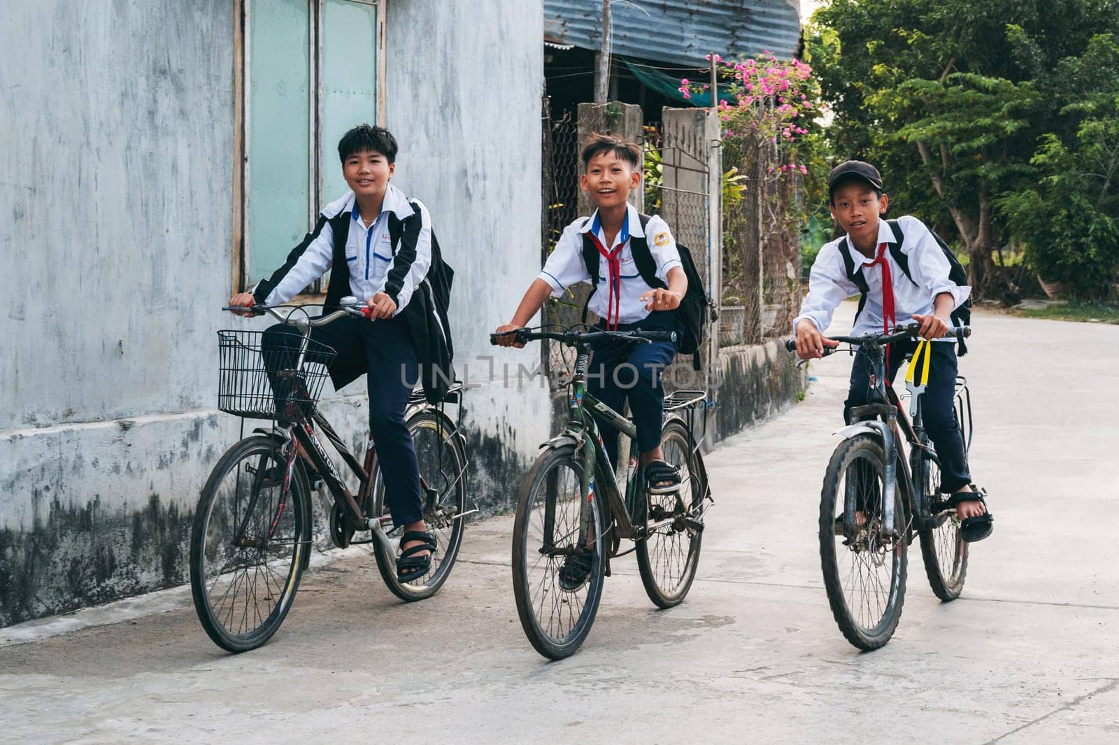 Happy Asian Vietnamese children school boys friends in school uniforms riding bicycles in the village. An Cu, Tuy An, Phu Yen province, Vietnam - April 14, 2025