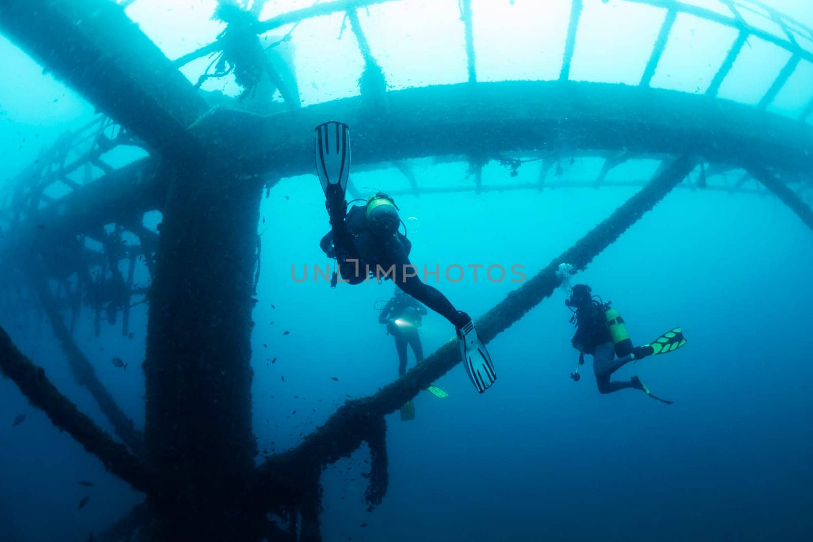 unrecognizable divers diving next to the structure of a sunken wreck in the sea, concept of scuba diving and underwater adventure