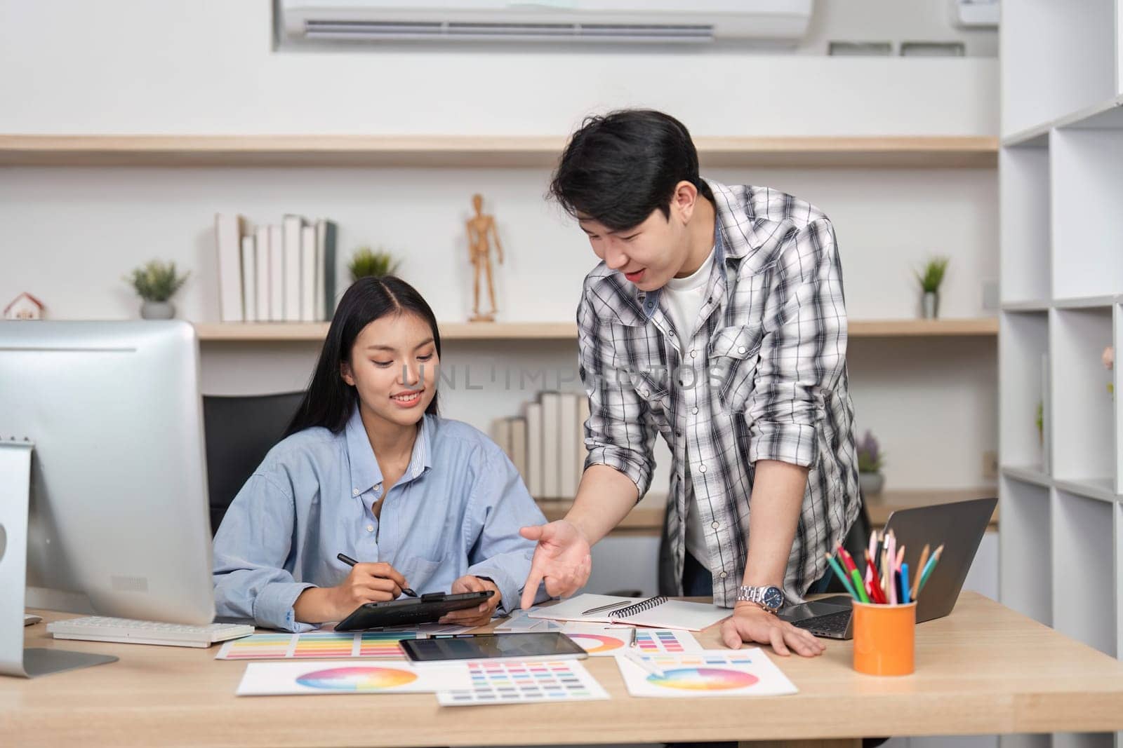 A young woman and man discuss UIUX design elements while working on tablets and computers in a stylish office environment.