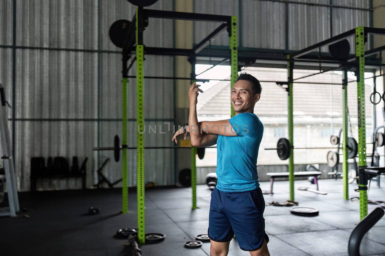 A cheerful male athlete stretches in a gym, showcasing positivity and motivation in fitness training.
