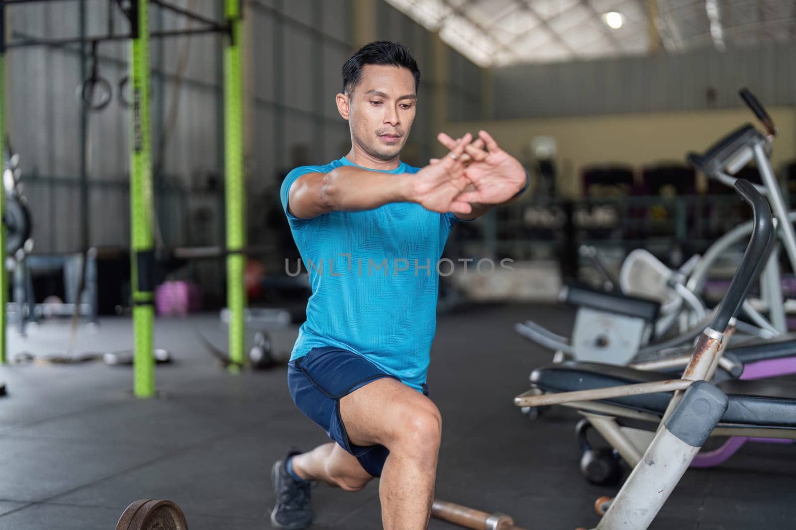 A dedicated man performs lunges in a gym, emphasizing strength training and preparation for an intense workout.